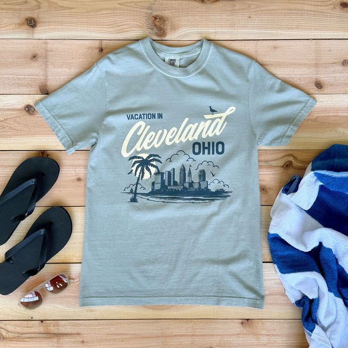 Gray t-shirt with 'Vacation in Cleveland, Ohio' design on a wooden surface with flip-flops and a towel.