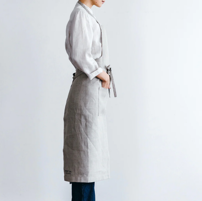 Side view of the Field Company linen full length apron in natural gray, tied at the waist over a white shirt
