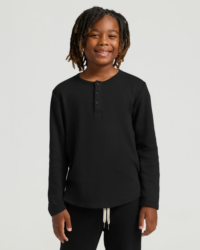 Child wearing Boys' All Black Waffle Long Sleeve Henley, smiling.