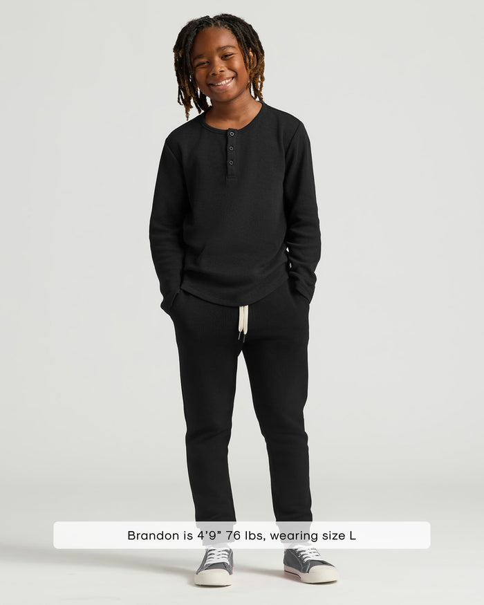 Boy wearing Boys' Waffle Long Sleeve Henley 3-Pack, smiling hands in pockets.