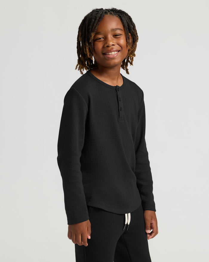 Boy wearing Boys Black Long Sleeve Waffle Henley, smiling confidently.