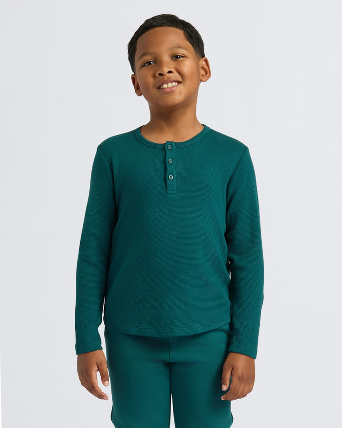 Boy wearing Boys' Waffle Long Sleeve Henley, deep teal, smiling gently, arms relaxed.