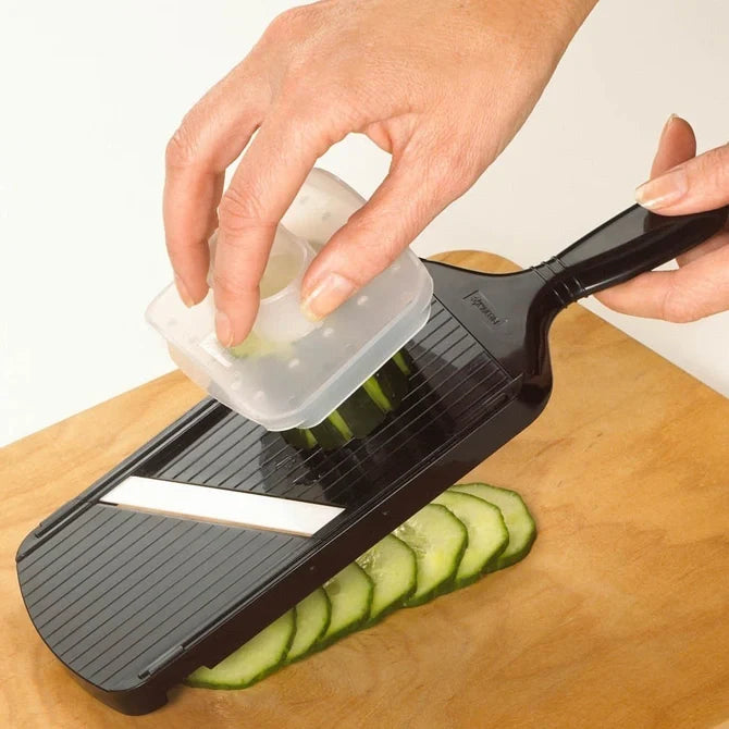 Person using a mandoline slicer to slice cucumbers on a wooden cutting board.