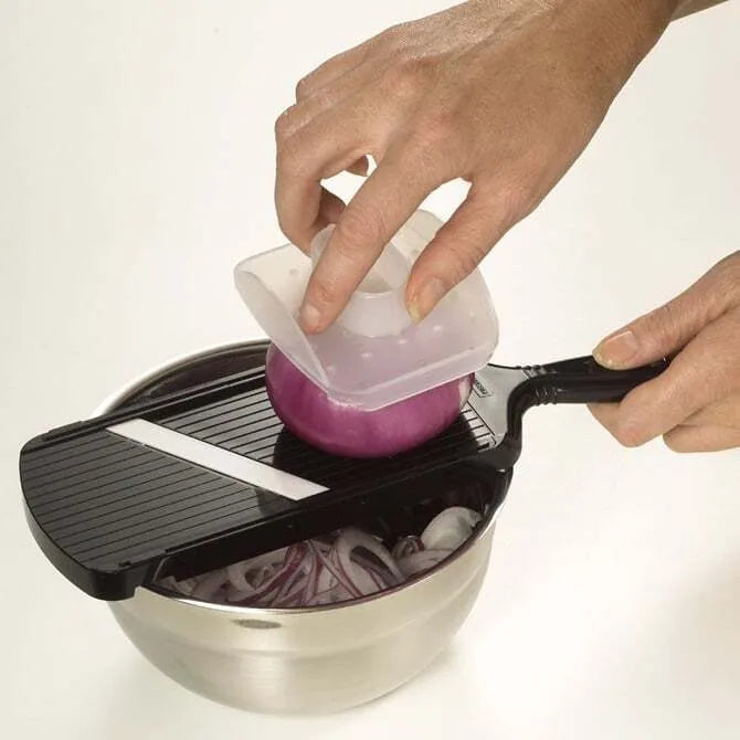 Person using a mandoline slicer to slice onion into a silver bowl.