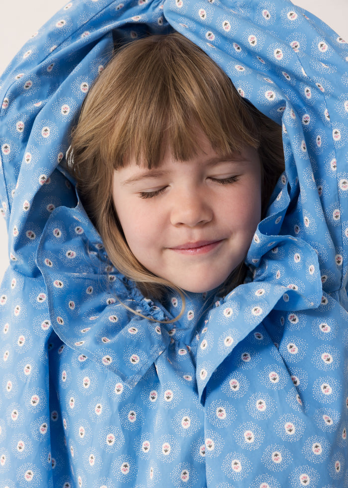 Child wearing a blue dress with a floral print and lace detail.