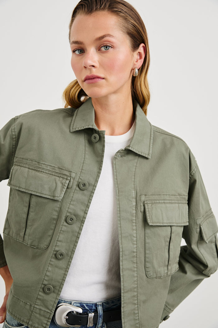 Madison Jacket with Button Closure, Two Chest Flap Pockets, Two Sleeve Flap Pockets, Adjustable Button Tab at Cuffs, and a Button Tab at Hem in Dark Olive Colorway - Front View Featured on Model