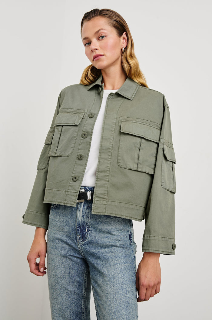 Madison Jacket with Button Closure, Two Chest Flap Pockets, Two Sleeve Flap Pockets, Adjustable Button Tab at Cuffs, and a Button Tab at Hem in Dark Olive Colorway - Front View Featured on Model