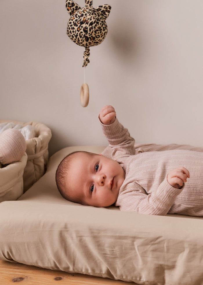 Leopardmønstret musikuro over sengen; baby i lys beige heldragt
