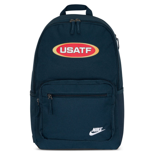 A navy blue Nike Sportswear Heritage backpack with a prominent USATF logo on the front, featuring multiple compartments and padded shoulder straps.