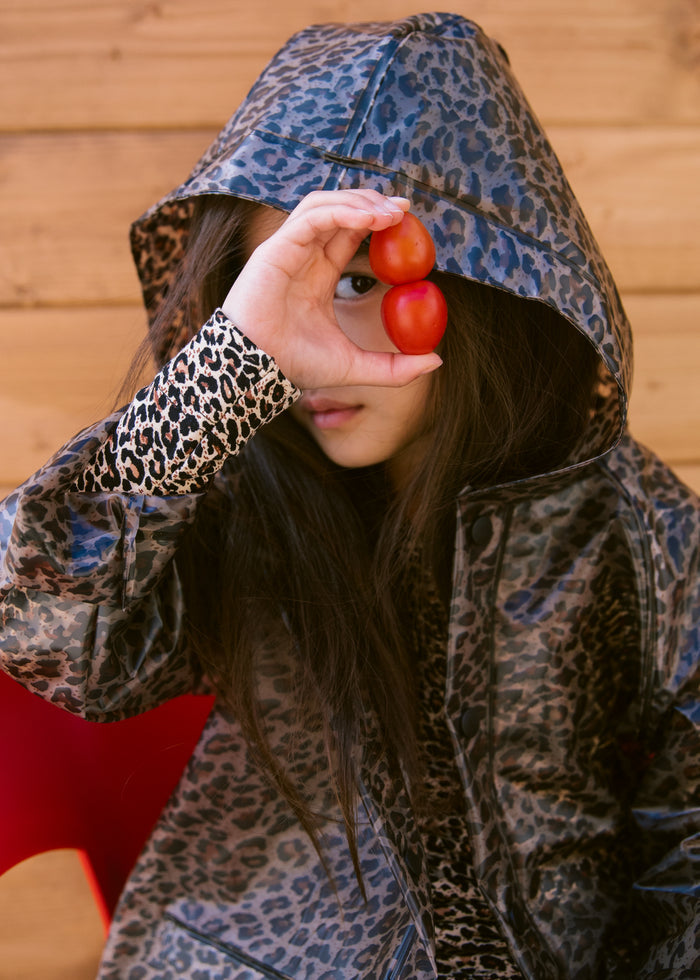 Child wearing leopard print hooded raincoat, looking through a piece of tomato