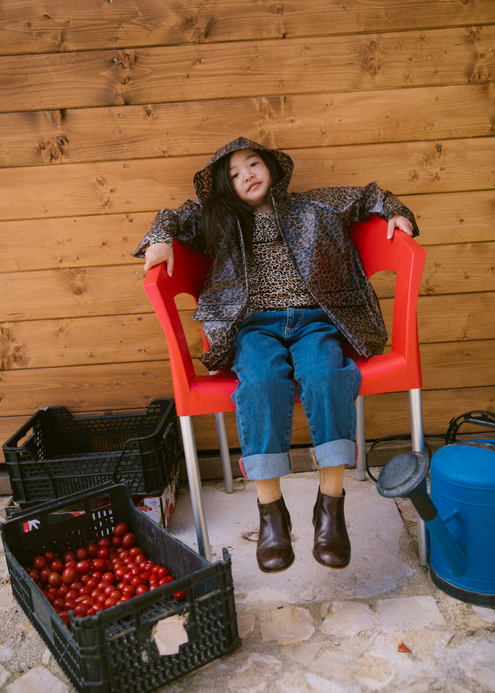 Child sitting on a red chair wearing a leopard print raincoat and jeans