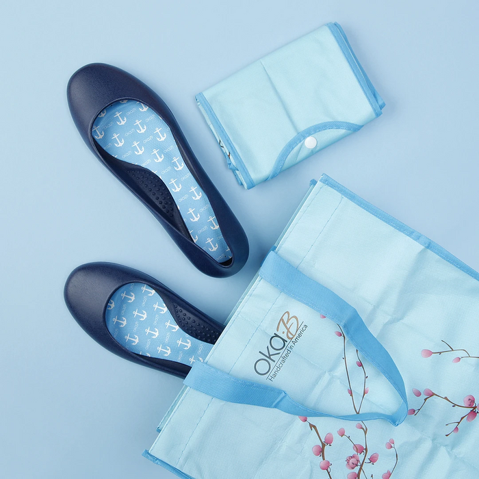 Blue Oka-B Reusable Shopping Bag | Oka-B with floral design, folded compactly next to a pair of navy blue shoes with anchor-patterned insoles on a light blue background.