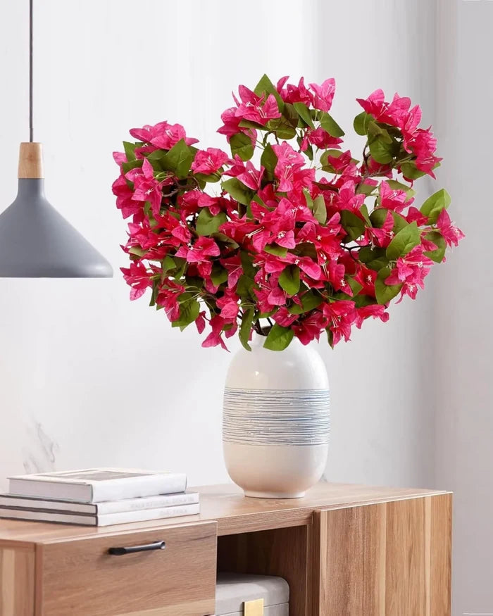Artificial bougainvillea stems with vivid pink flowers and green leaves in a white vase