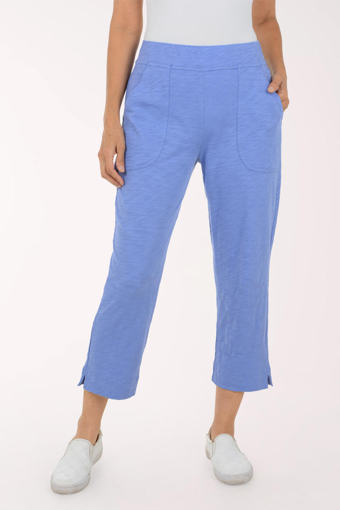 A model wearing a pair of light blue cropped pants with side slits and front patch pockets, paired with white slip-on shoes against a plain white studio background.