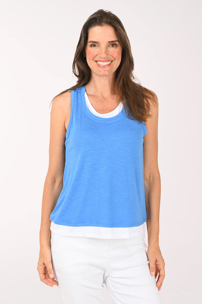 Woman wearing a blue sleeveless top and white pants on a white background