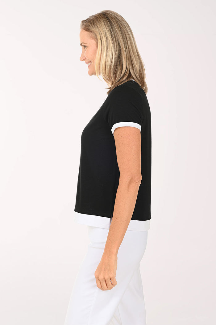 Woman wearing a black top with white trim and white pants on a white background
