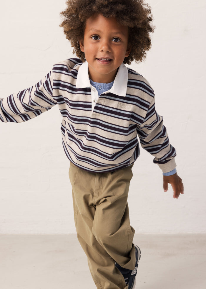 Child wearing a striped sweat polo and brown pants.