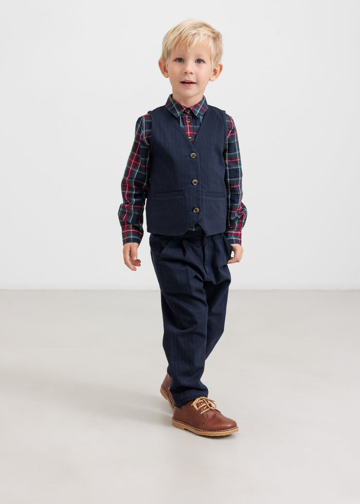 Boy wearing dark blue party pants and vest with checkered shirt in a Christmas look for children